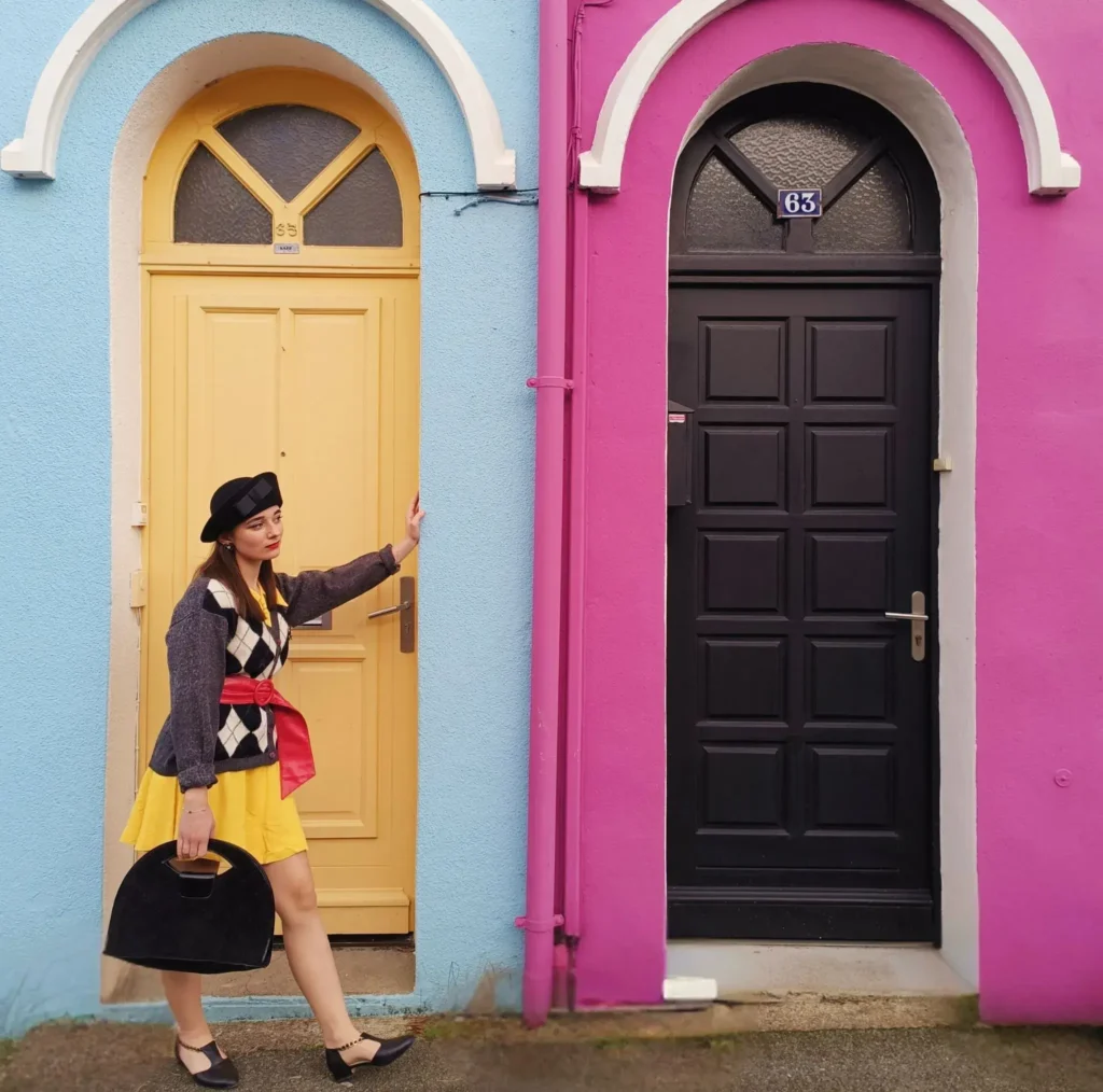 Femme chic au chapeau noir vintage devant deux portes de maisons colorées.