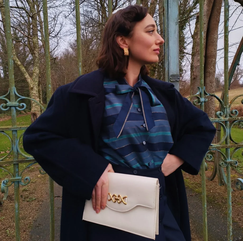 Femme vintage style années 50 vêtue de bleu et une pochette blanc crème à la main.