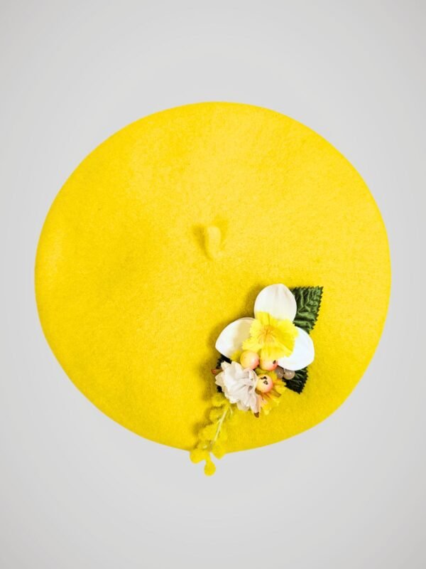 Béret en laine jaune orné d'une broche modèle jonquille fait main, vue de face.