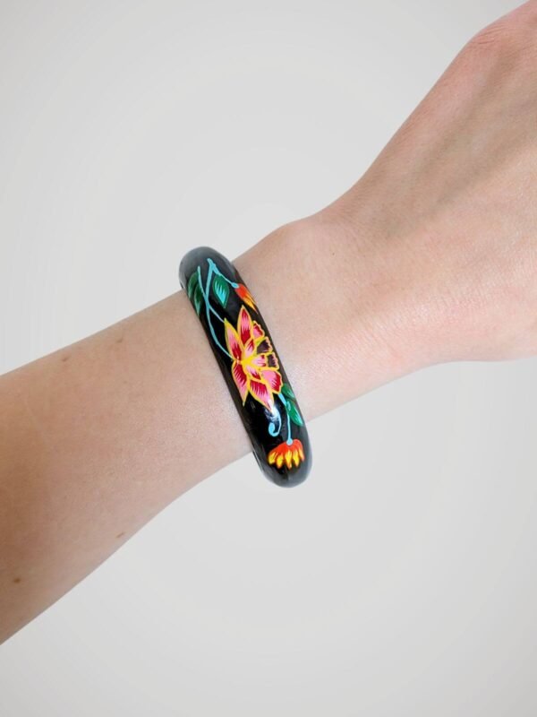 Bracelet jonc vintage noir peint à la main de motifs floraux colorés, en bois, porté et vue de face.