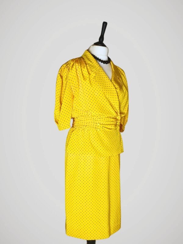 Ensemble composé d'une jupe tailleur et d'un chemisier manches courtes, vintage des années 80, jaune à pois noirs pour femme, taille M à L, vue de côté.